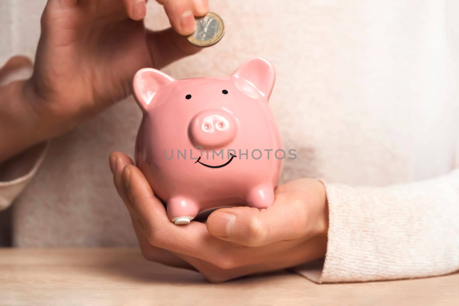 Women's hands carefully hold the piggy bank to preserve wealth, savings and financial success. A girl puts a coin in a piggy bank.