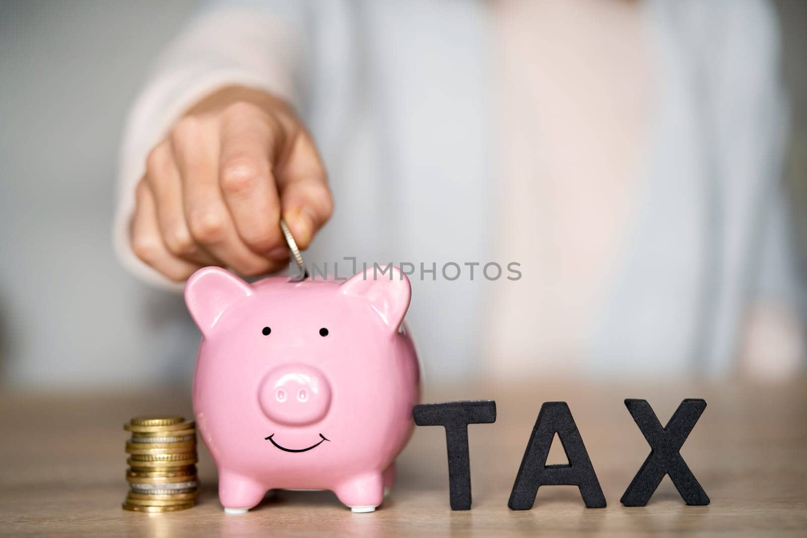 The hand of a young girl puts letters on the table with the words "tax" next to a piggy bank on the table at her workplace, close up view.