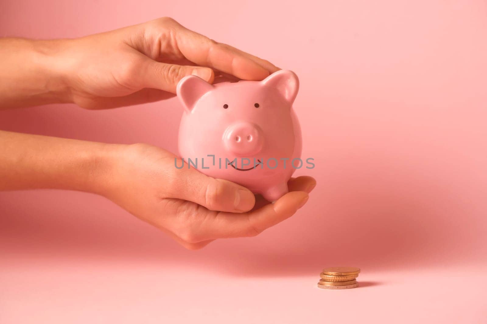 Women's hands carefully hold the piggy bank to preserve wealth, savings and financial success. A girl puts a coin in a piggy bank.