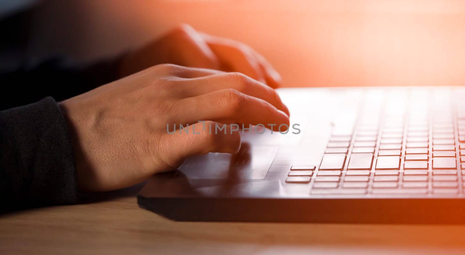 Male hands with a sun effect are typing on a laptop keyboard, close-up view. A man works in an office, is engaged in the development of his business at home, writes messages online.