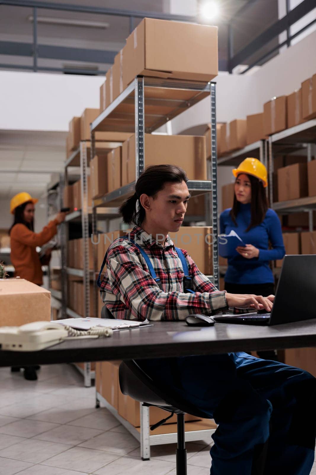 Logistics manager planning goods supply on laptop in freight warehouse. Young asian shipment service employee typing on computer and checking inventory management system in storehouse