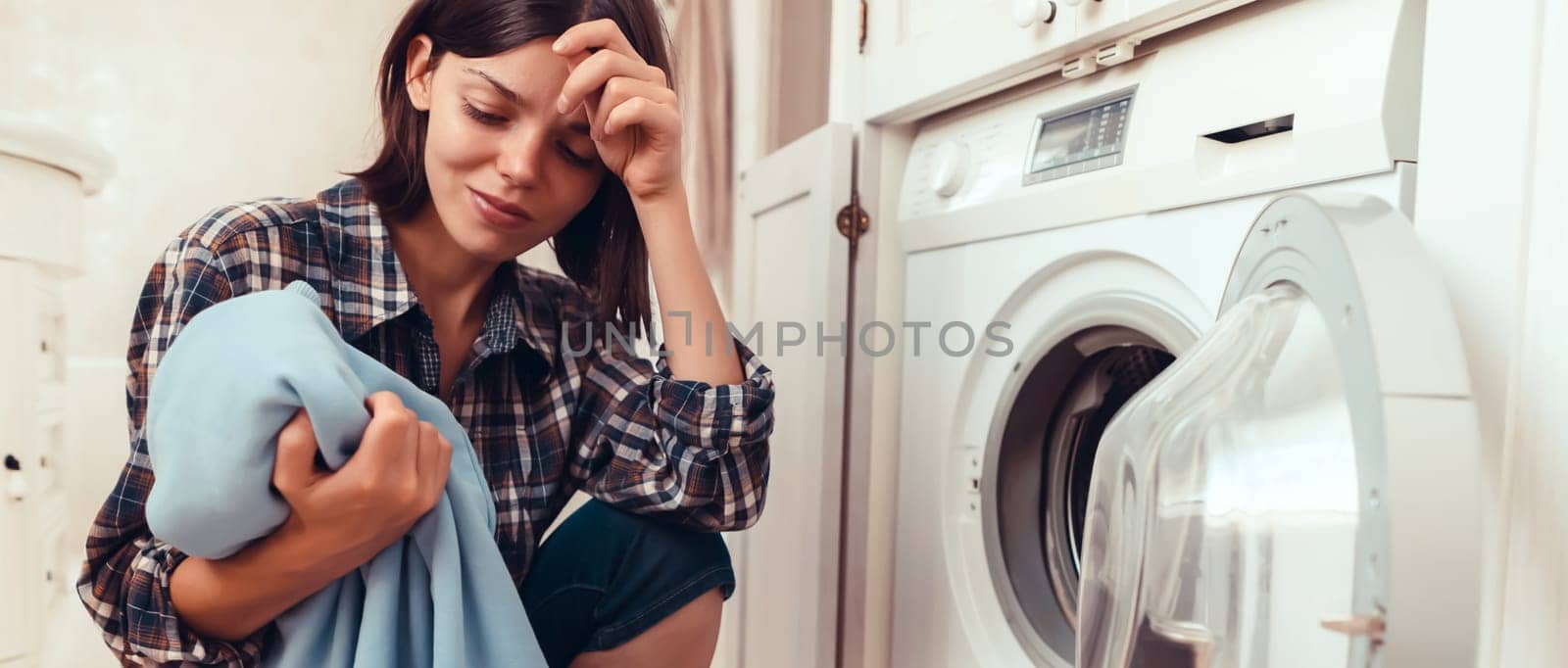 A young girl puts things in the washing machine, a tired woman sits on the floor of a cozy house and looks at the stain on her jacket, which needs to be removed with detergent.