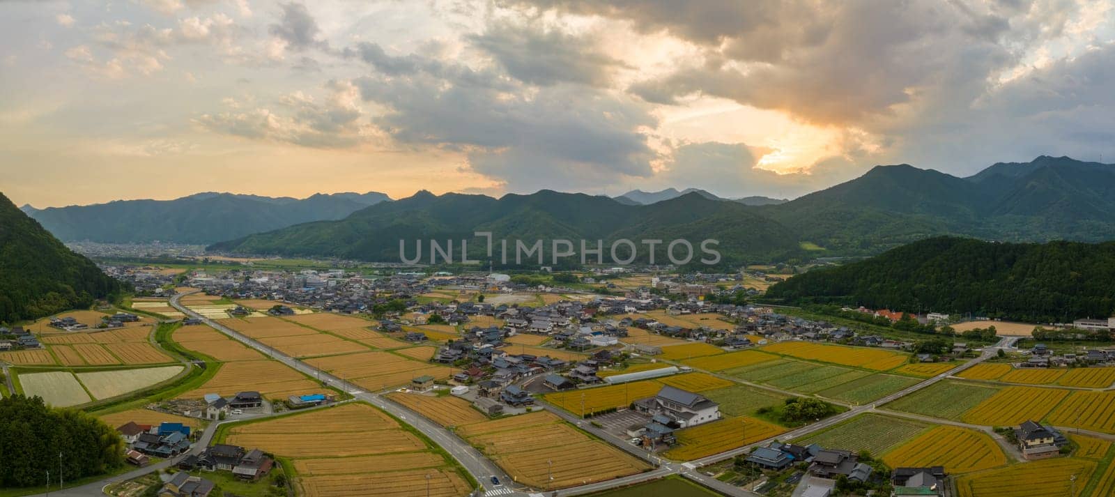 Golden wheat fields and small farming village by mountains at sunset by Osaze