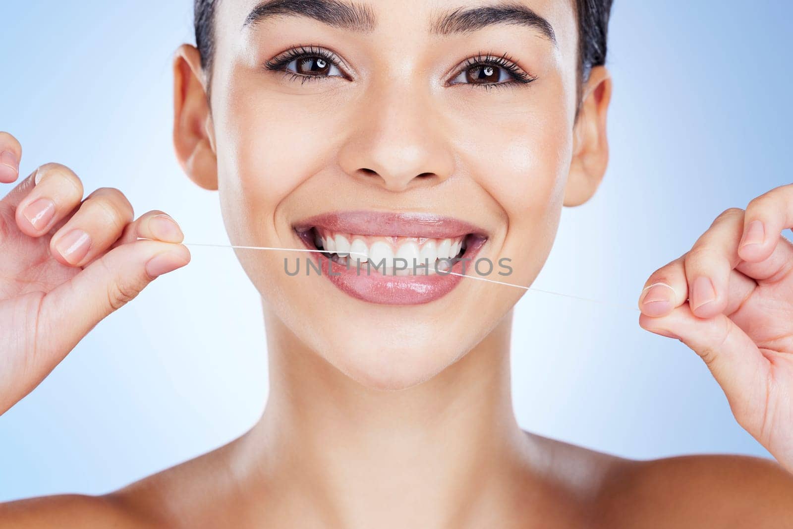 Face, flossing teeth and dental with woman, hygiene and beauty with grooming and mouth care on blue background. Hands, string and healthy gums with fresh breath, health and skin glow in portrait.