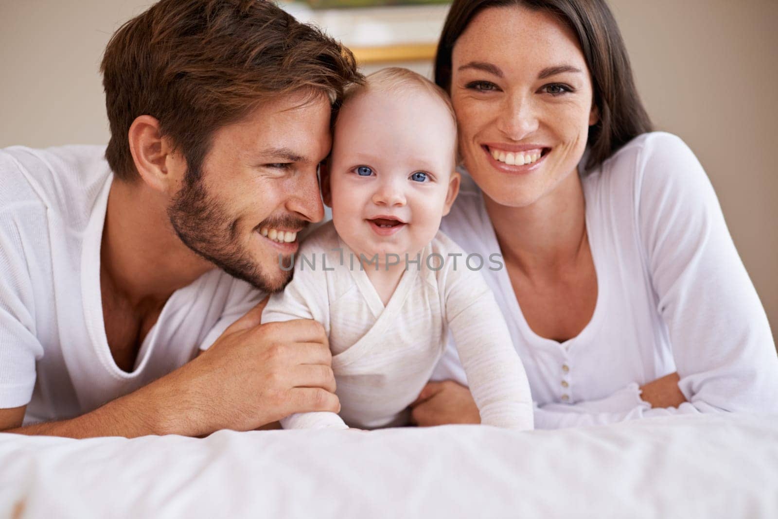 Portrait, happy family and parents with baby on bed for love, care and quality time together at home. Mother, father and newborn child relaxing in bedroom for development, caring support or happiness by YuriArcurs