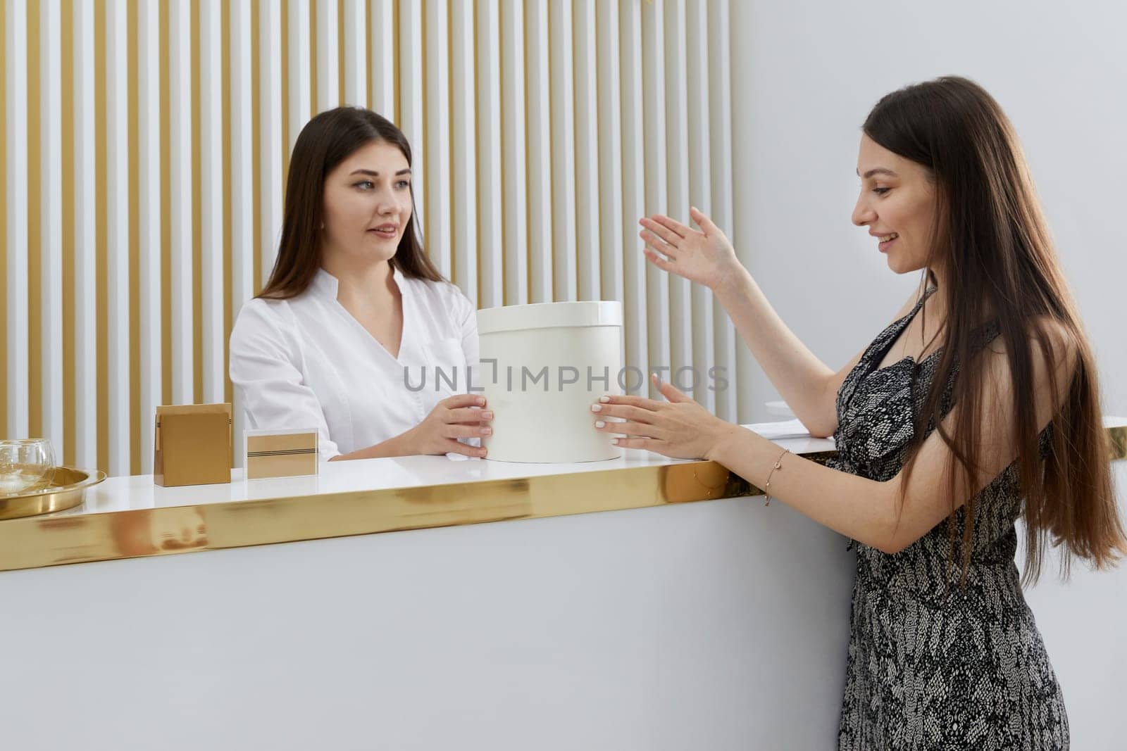 Female receptionist at reception desk with a client in a modern office. giving complementory present concept by Mariakray