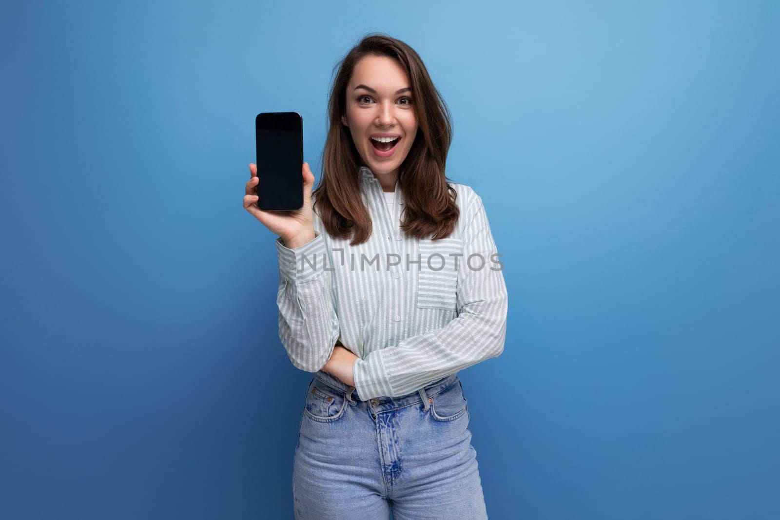 pretty young brunette woman in shirt showing smartphone mockup on studio background by TRMK