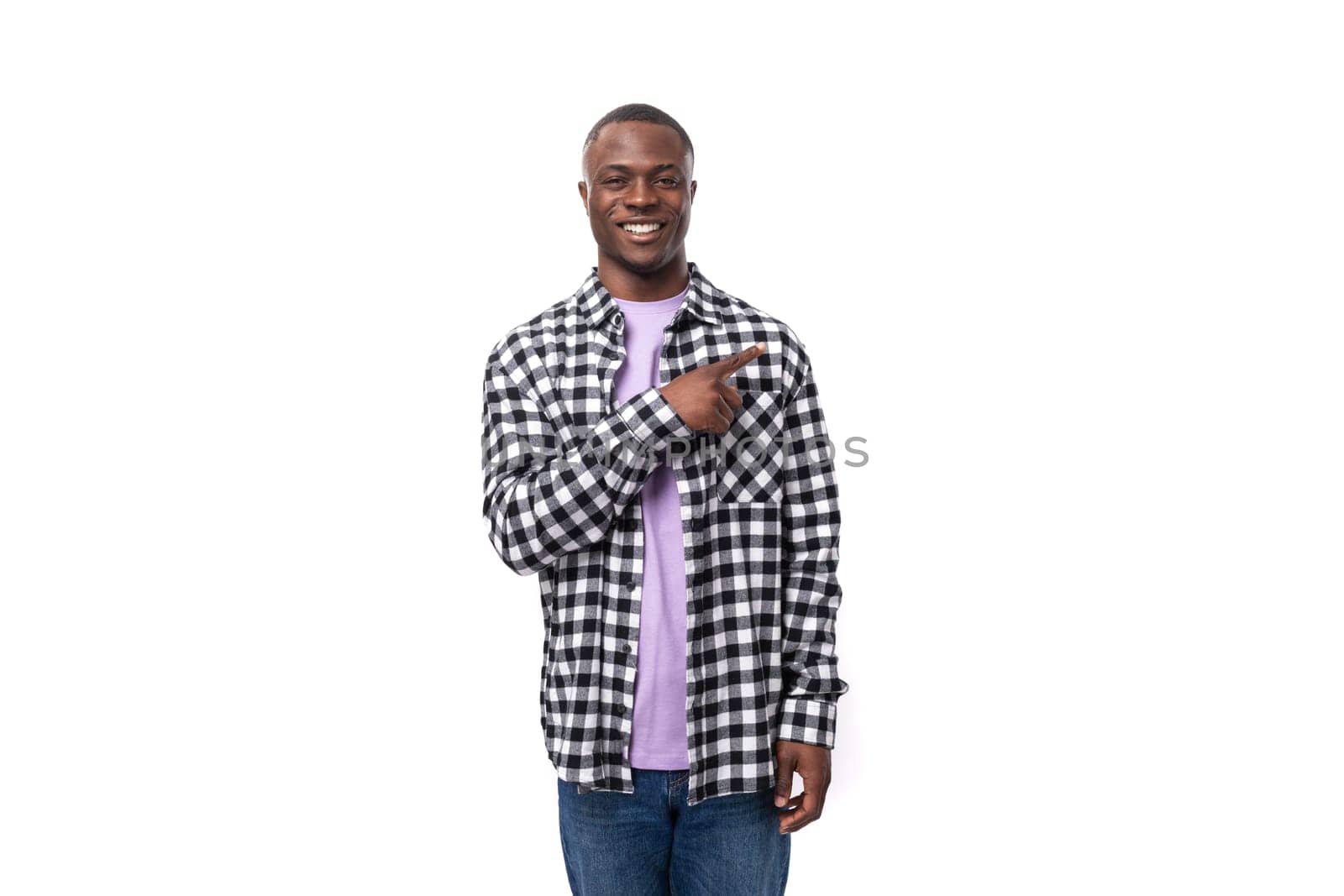 handsome 30 year old african guy dressed in a plaid black and white shirt points with his hand on the background with copy space.