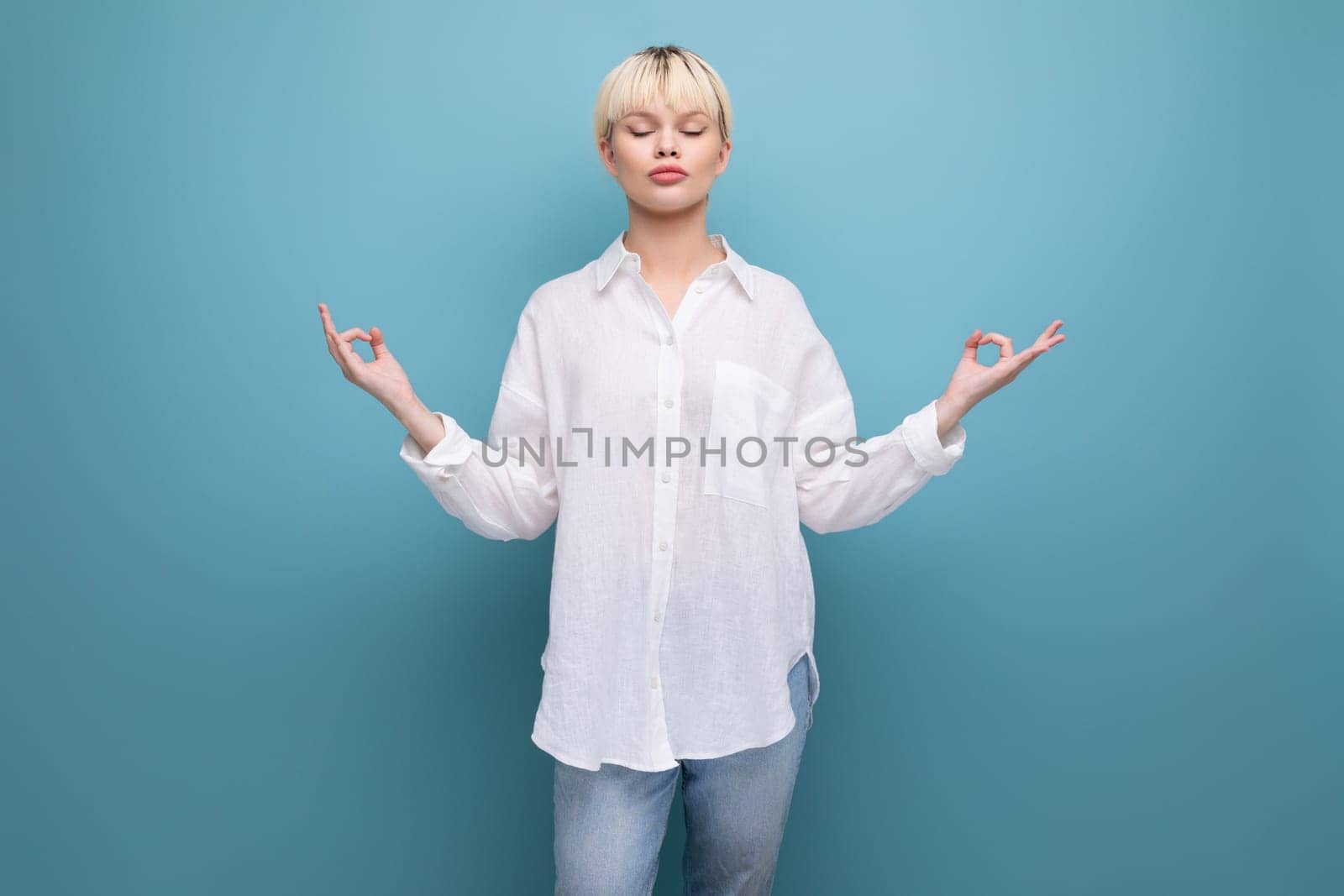 young calm pretty blonde businesswoman in a white shirt is meditating on the background with copy space. people lifestyle concept.