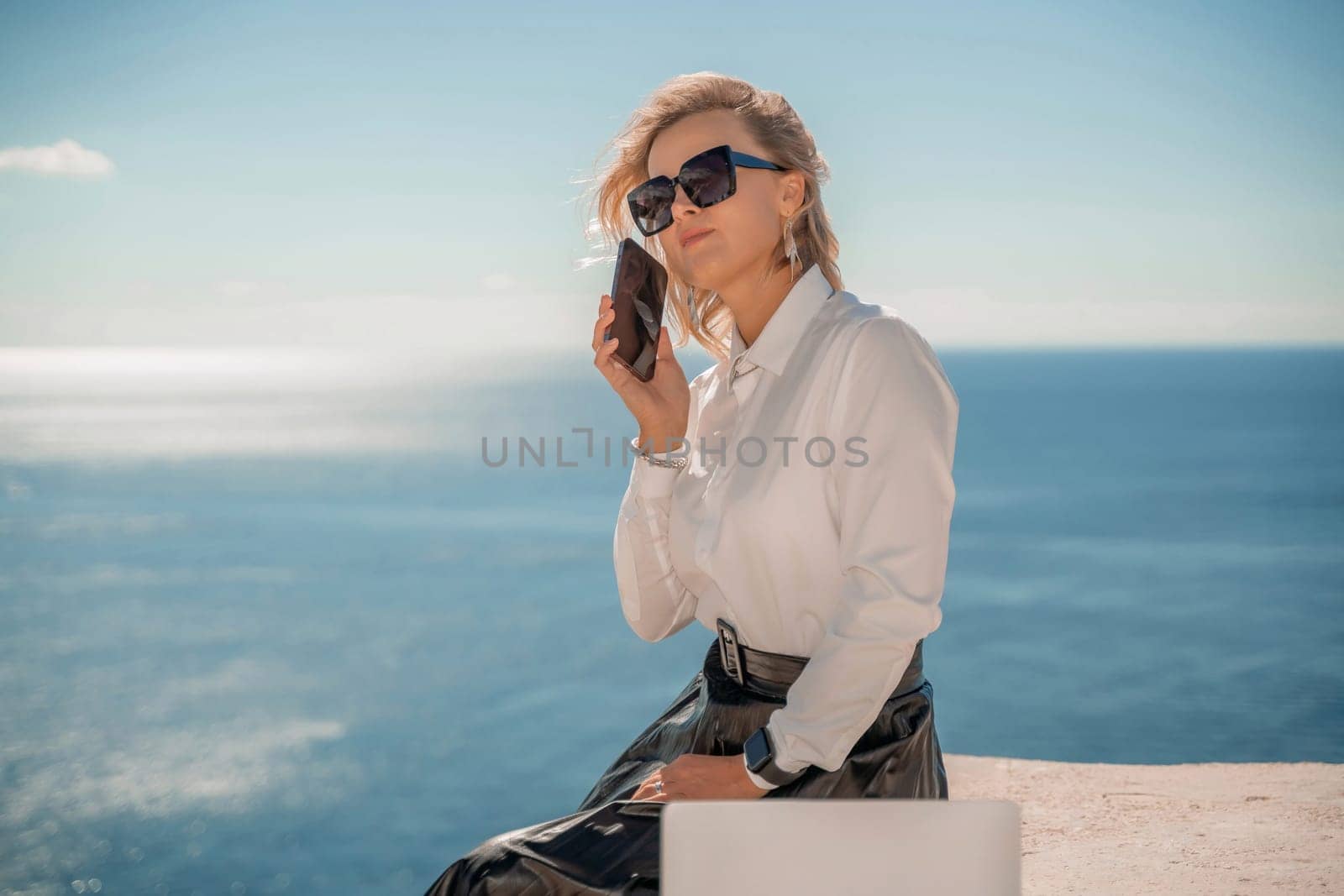 Freelance women sea working on a computer. Pretty middle aged woman with computer and phone outdoors with beautiful sea view. The concept of remote work. by Matiunina