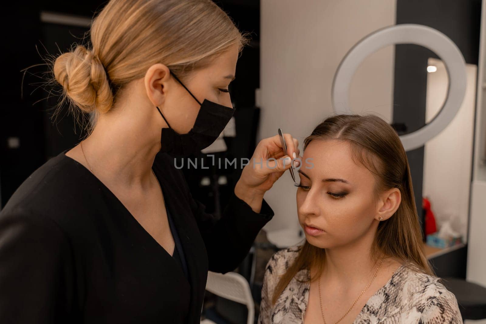 Makeup artist paints eyelashes to a woman in a beauty salon. by Matiunina