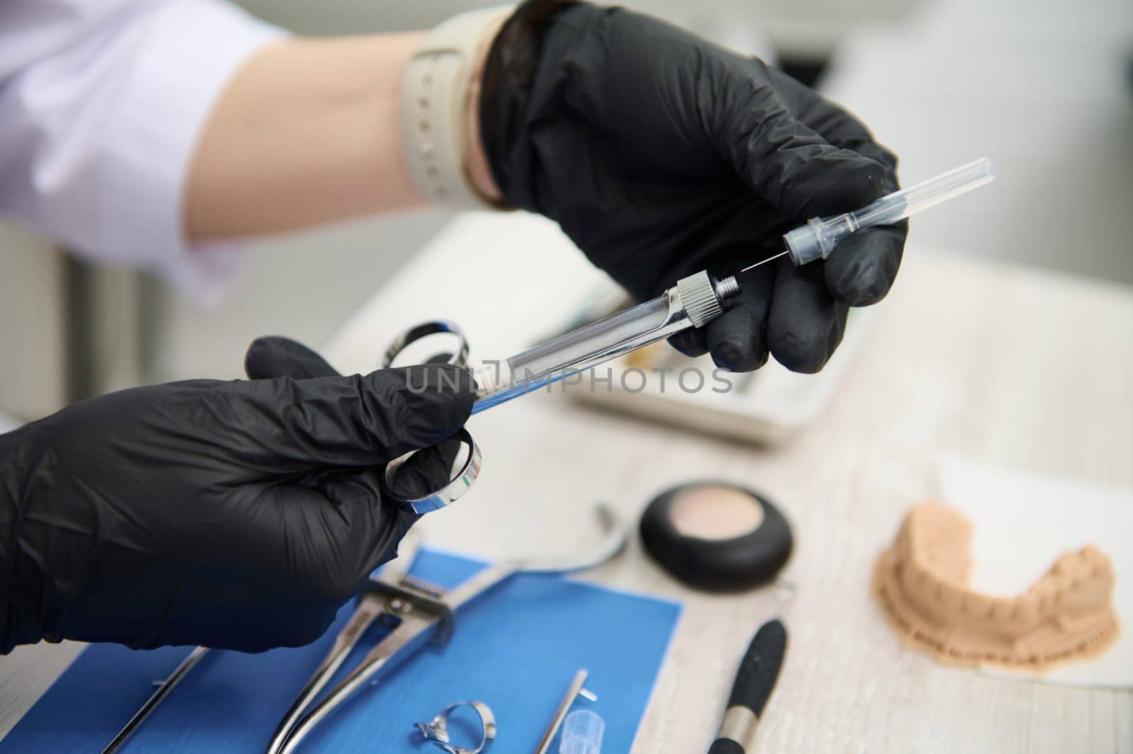 Close-up hands of a dentist in black surgical gloves, recharging cartridge with anesthetic in the stainless steel syringe, preparing dental anesthesia, sitting at table with tools used in dentistry
