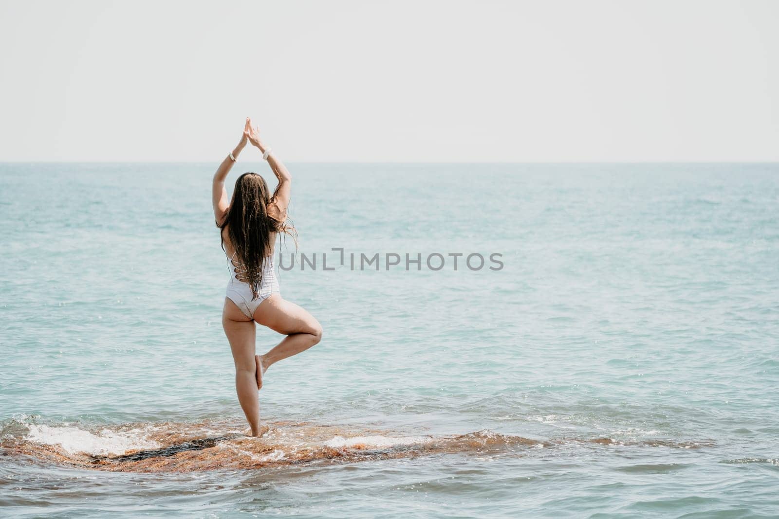 Woman sea yoga. Back view of free calm happy satisfied woman with long hair standing on top rock with yoga position against of sky by the sea. Healthy lifestyle outdoors in nature, fitness concept.