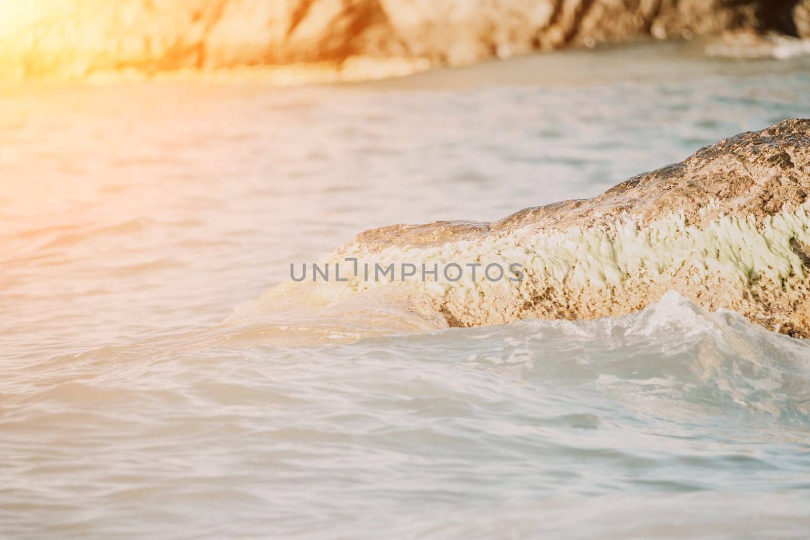 A red burning sunset with the silhouette of a cliff over the sea. Abstract nature summer or spring ocean sea background. Small waves on golden warm water surface with bokeh lights from sun.