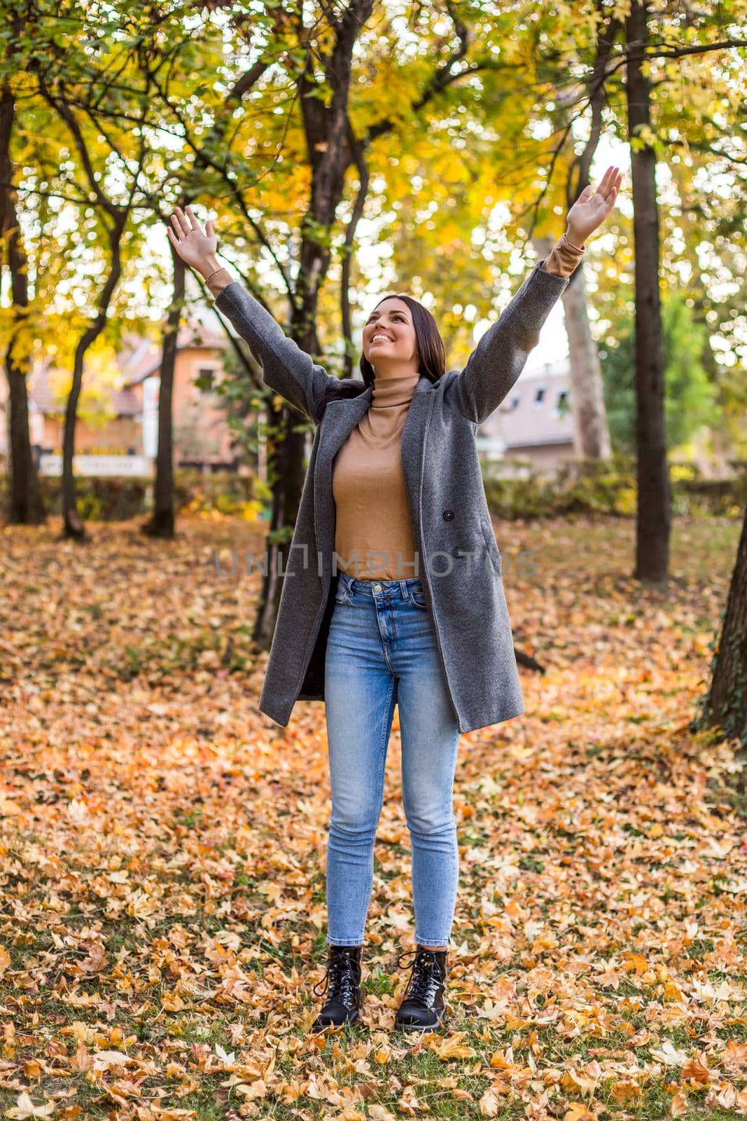 Beautiful woman standing in the park with her arms outstretched and enjoys in autumn.