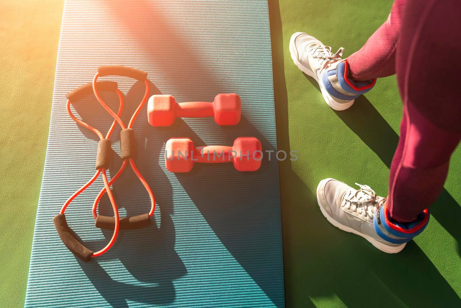 Woman legs near mat with expander and two dumbbells