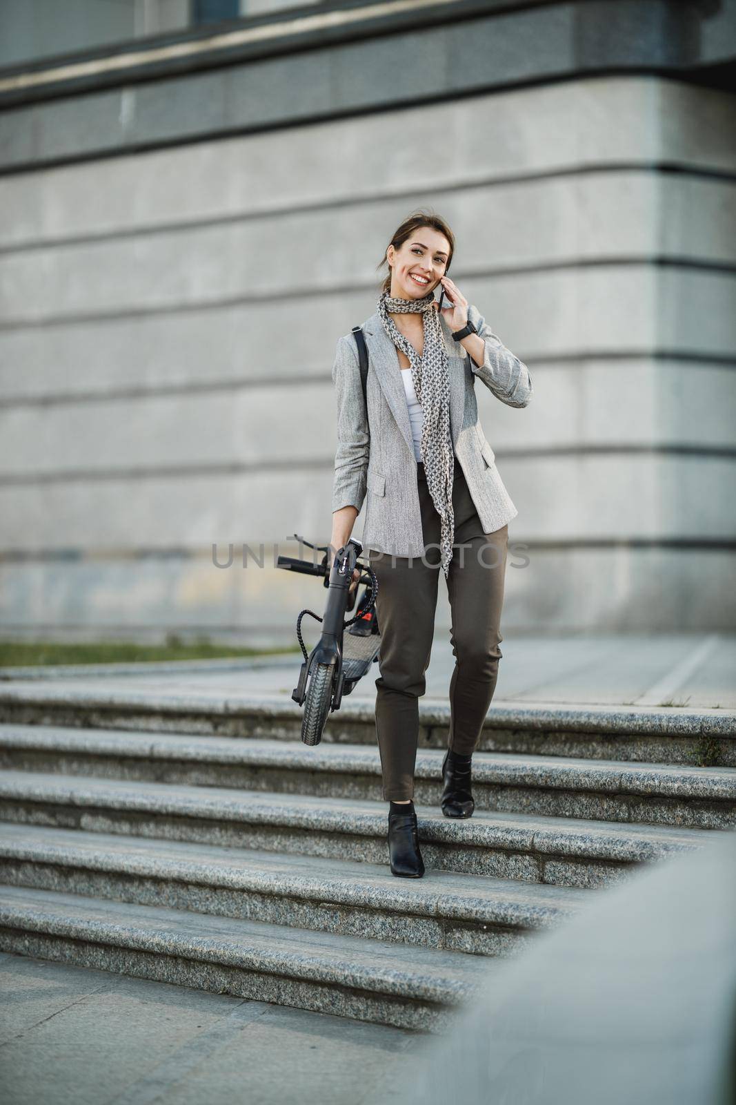 Shot of a young businesswoman talking on a smartphone while traveling with an electric scooter through the city.