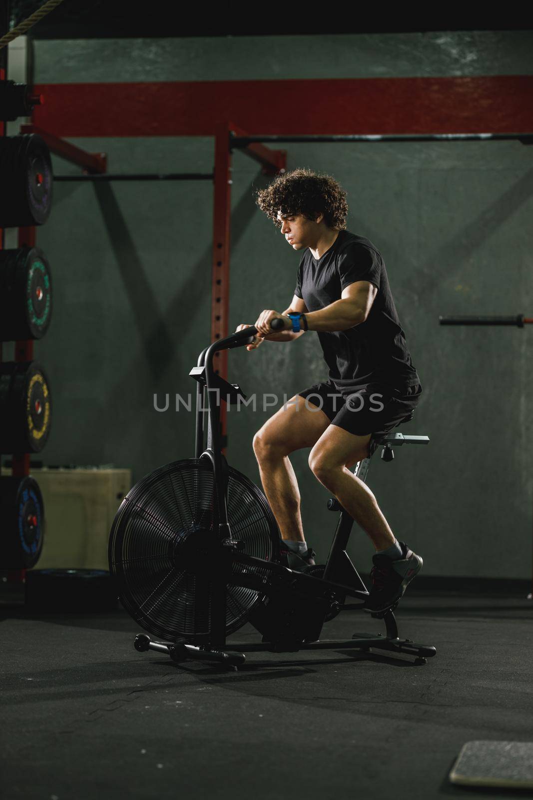 A muscular guy is doing hard cal bike crossfit training in the gym.