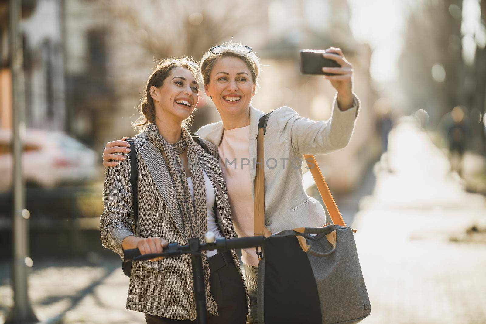 A two successful businesswomen taking a selfie with smartphone while walking through the city.