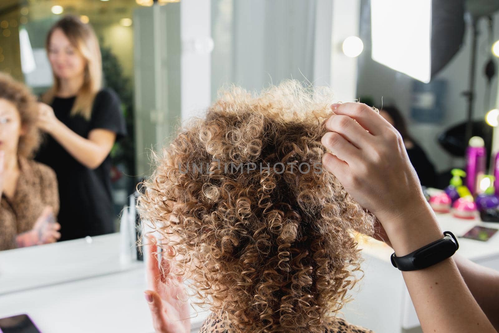 Hairdresser working with beautiful woman brown hair in hairdressing salon. Close up view of hand, curling iron and the appliance