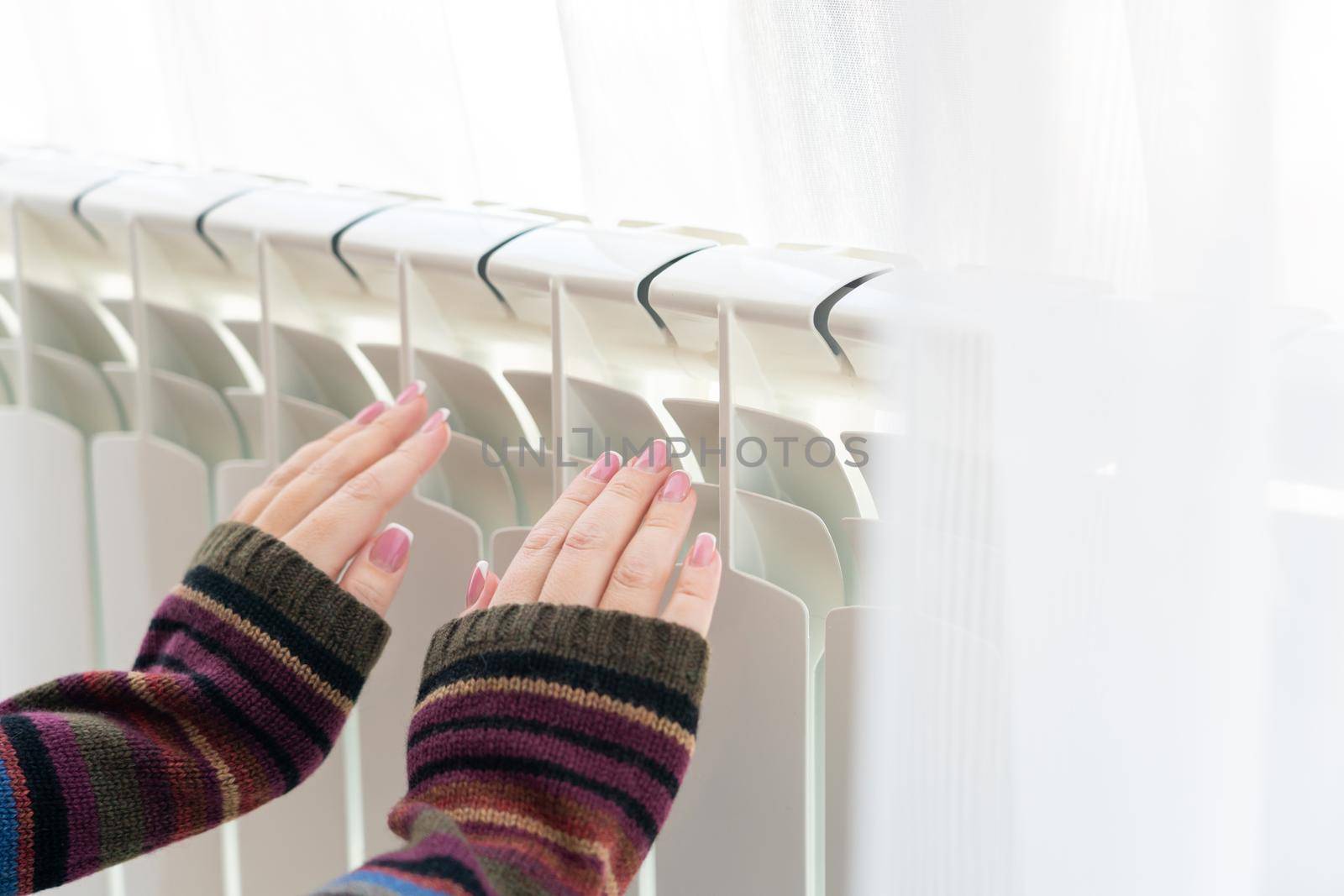 Girl warms up the frozen hands above hot radiator, close up