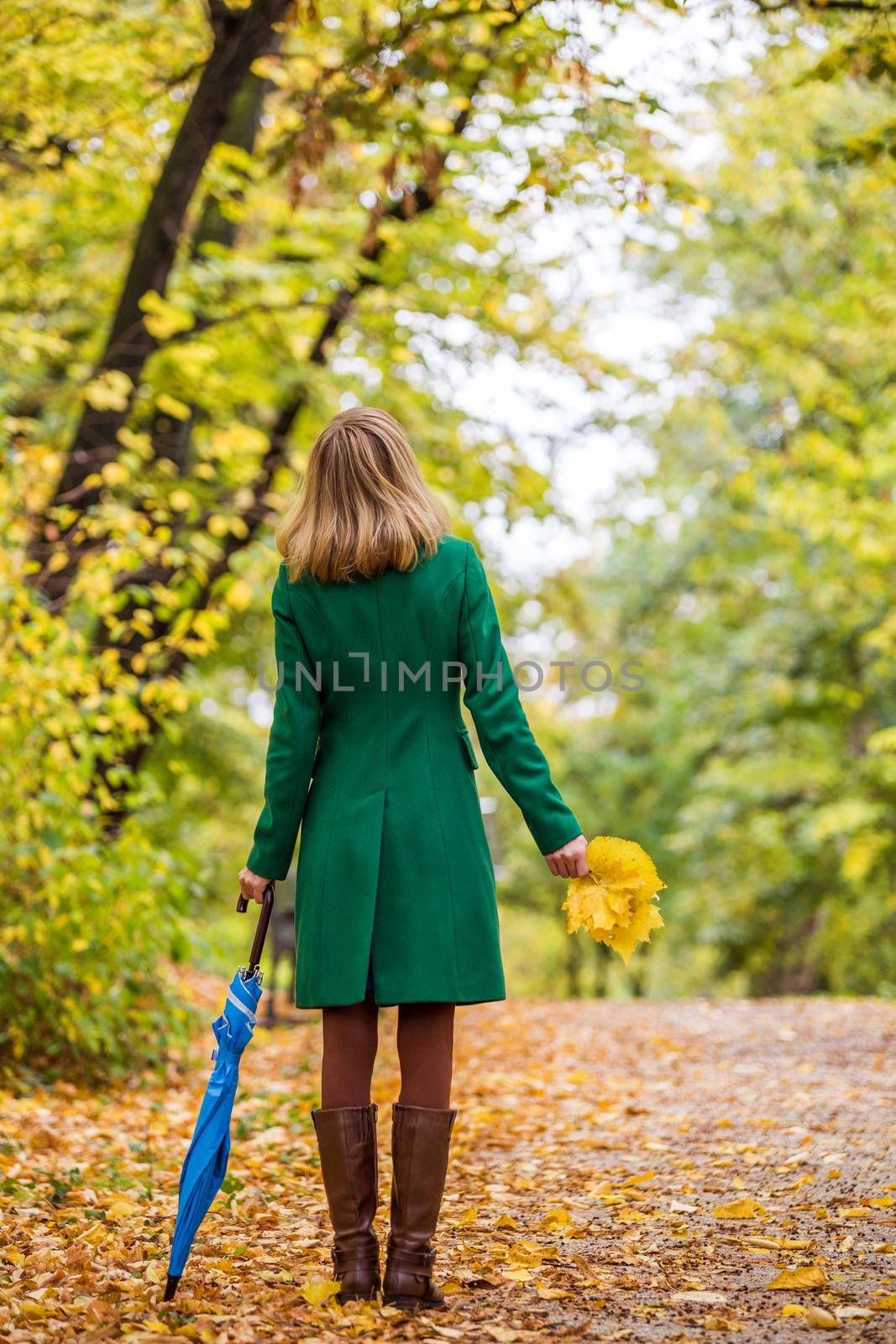Woman holding umbrella and fall leaves while standing in the park.