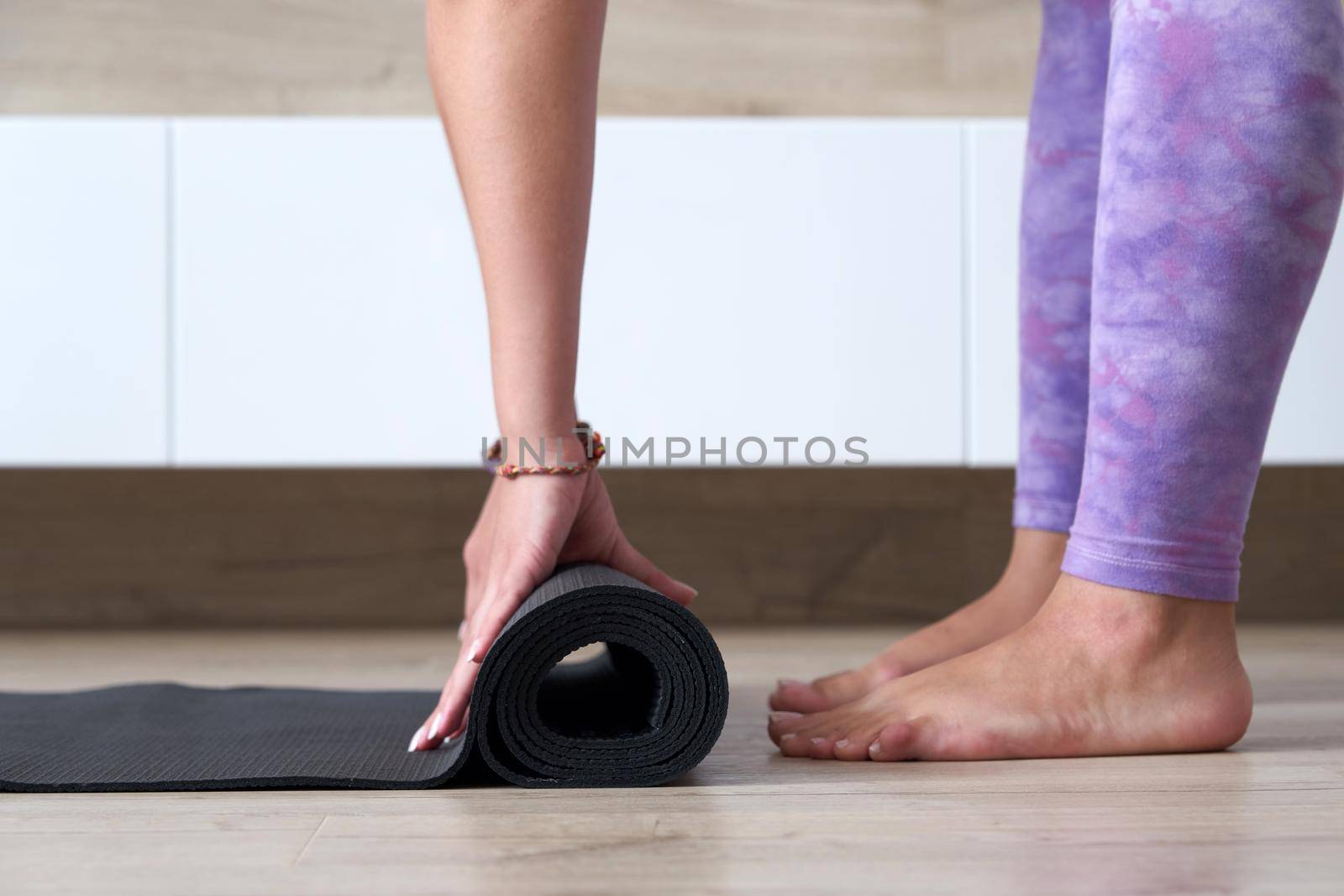 young woman folding black yoga or fitness mat after working out at home in living room