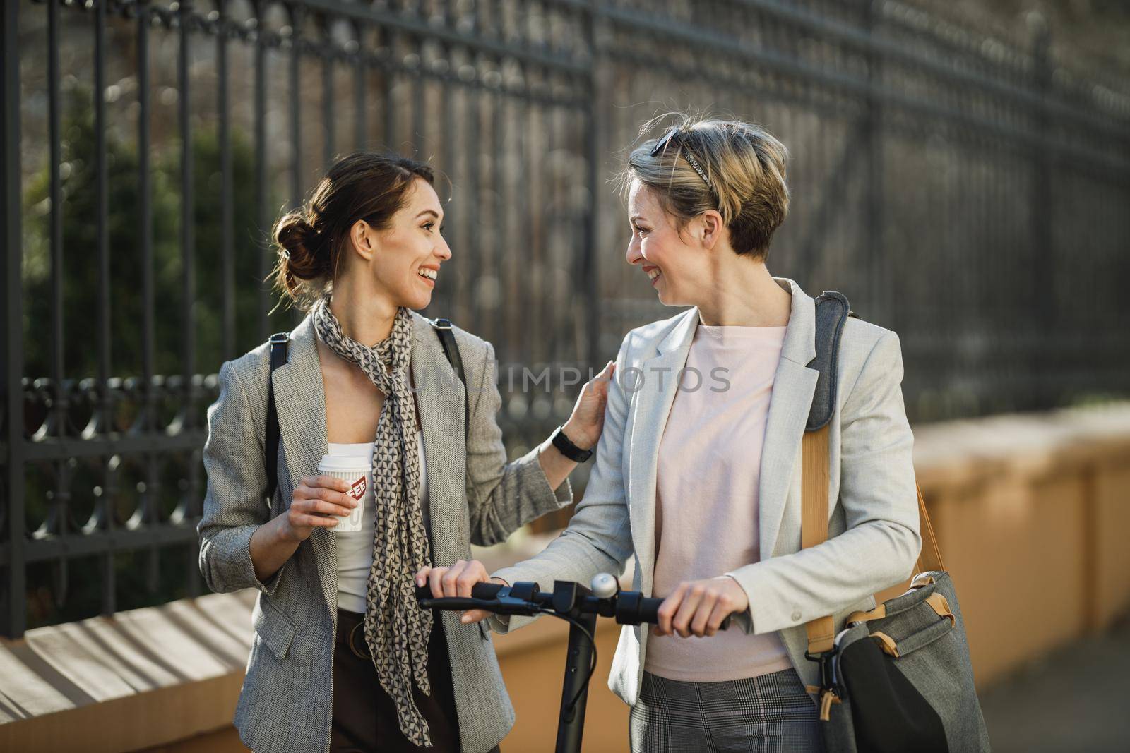 A two successful businesswomen having a quick coffee break and chatting while walking through the city.