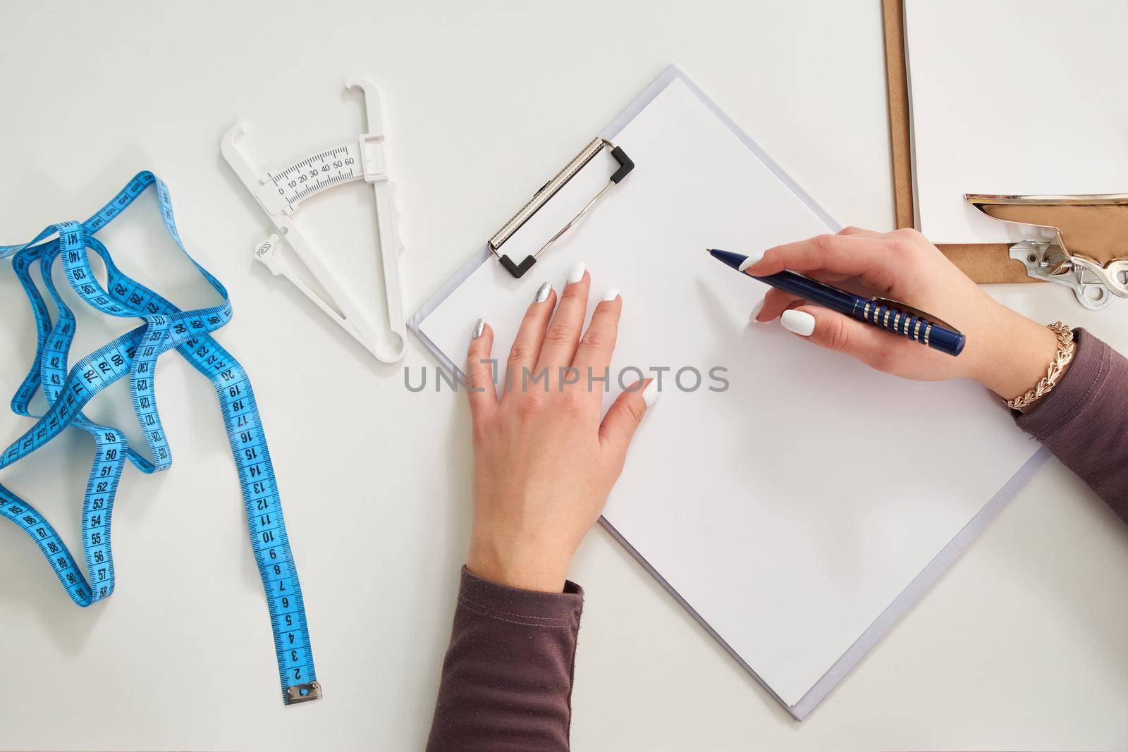 Nutritionist doctor writing diet plan on table with measuring tape, top view