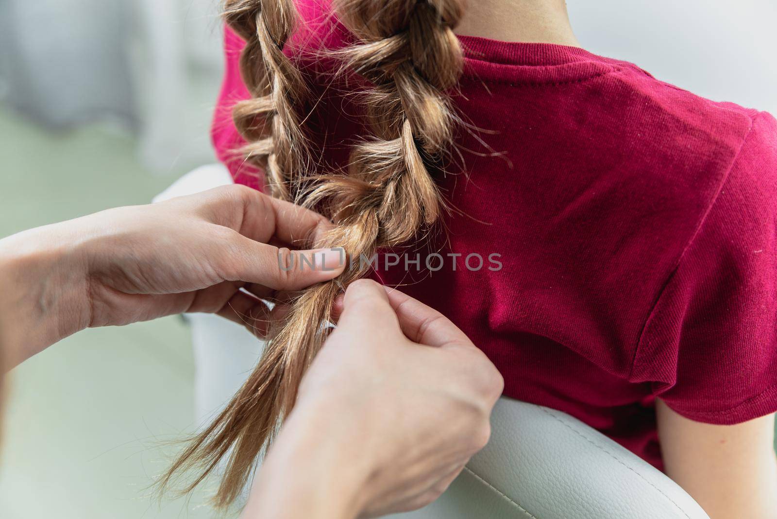 Hairdresser weaves a braid to a preteen blond girl