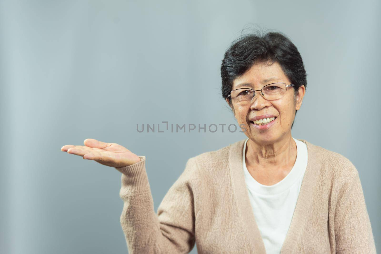 portrait of smiling old woman showing gesture with hand on gray background by Wmpix