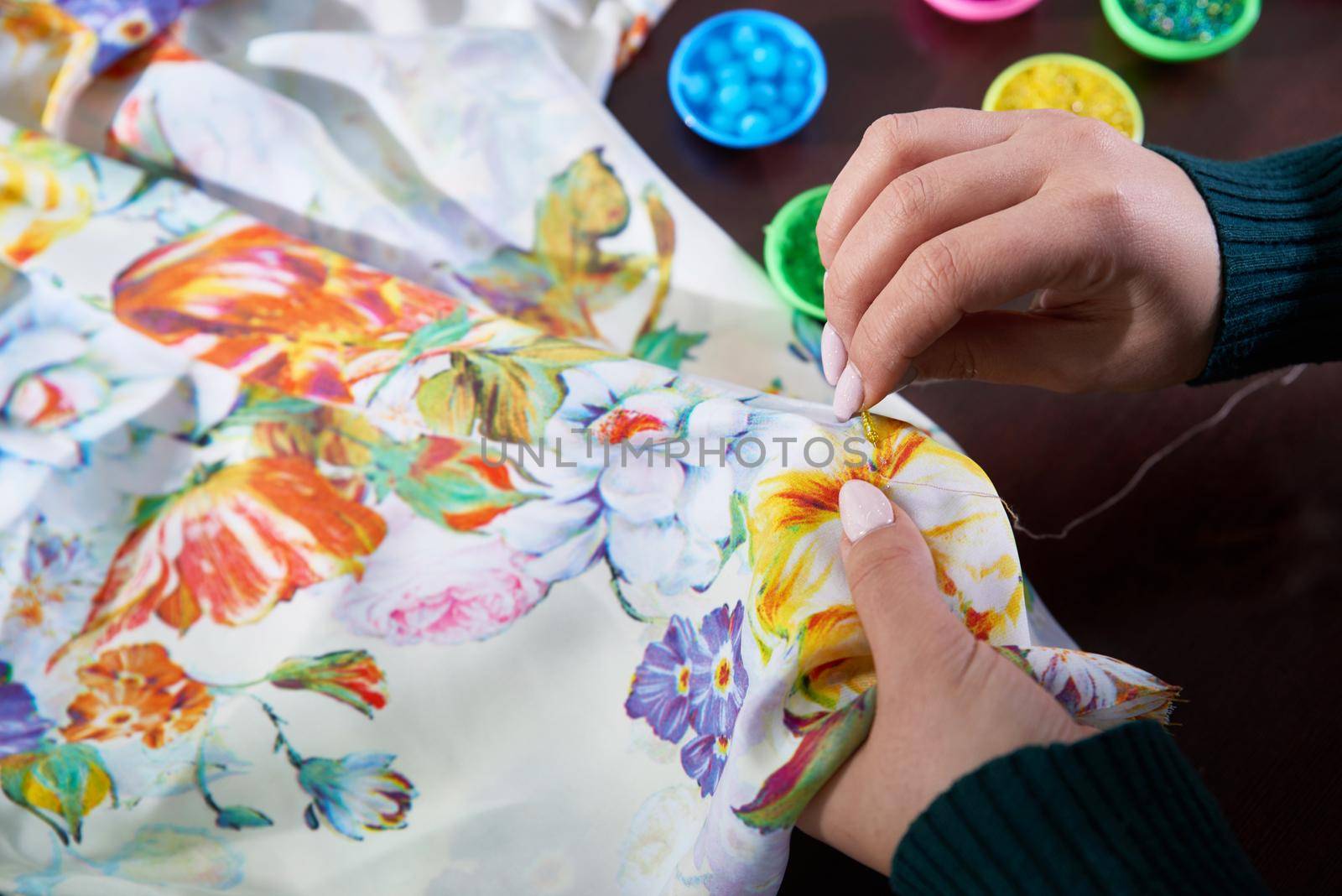 close-up hands of woman seamstress tailor ( dressmaker) designer wedding dress sews beads to lace on a blue background in the studio