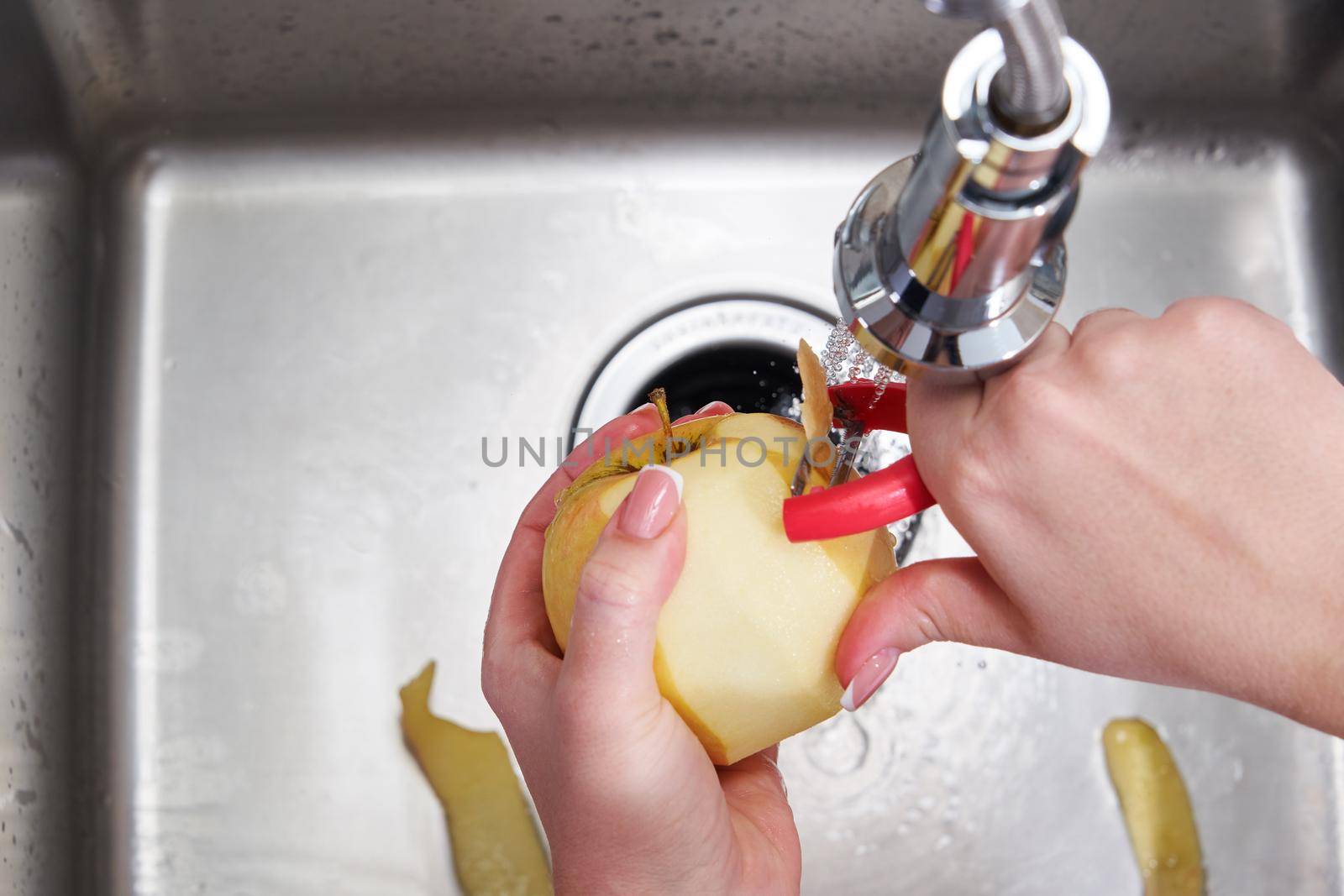 Cropped view of female hands peeling apple over Food waste disposer machine in modern kitchen