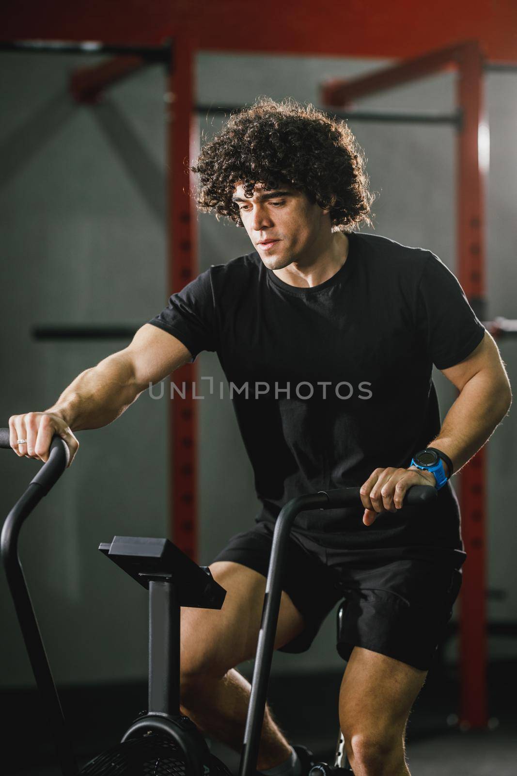 A handsome muscular man is doing hard cal bike crossfit training in the gym.