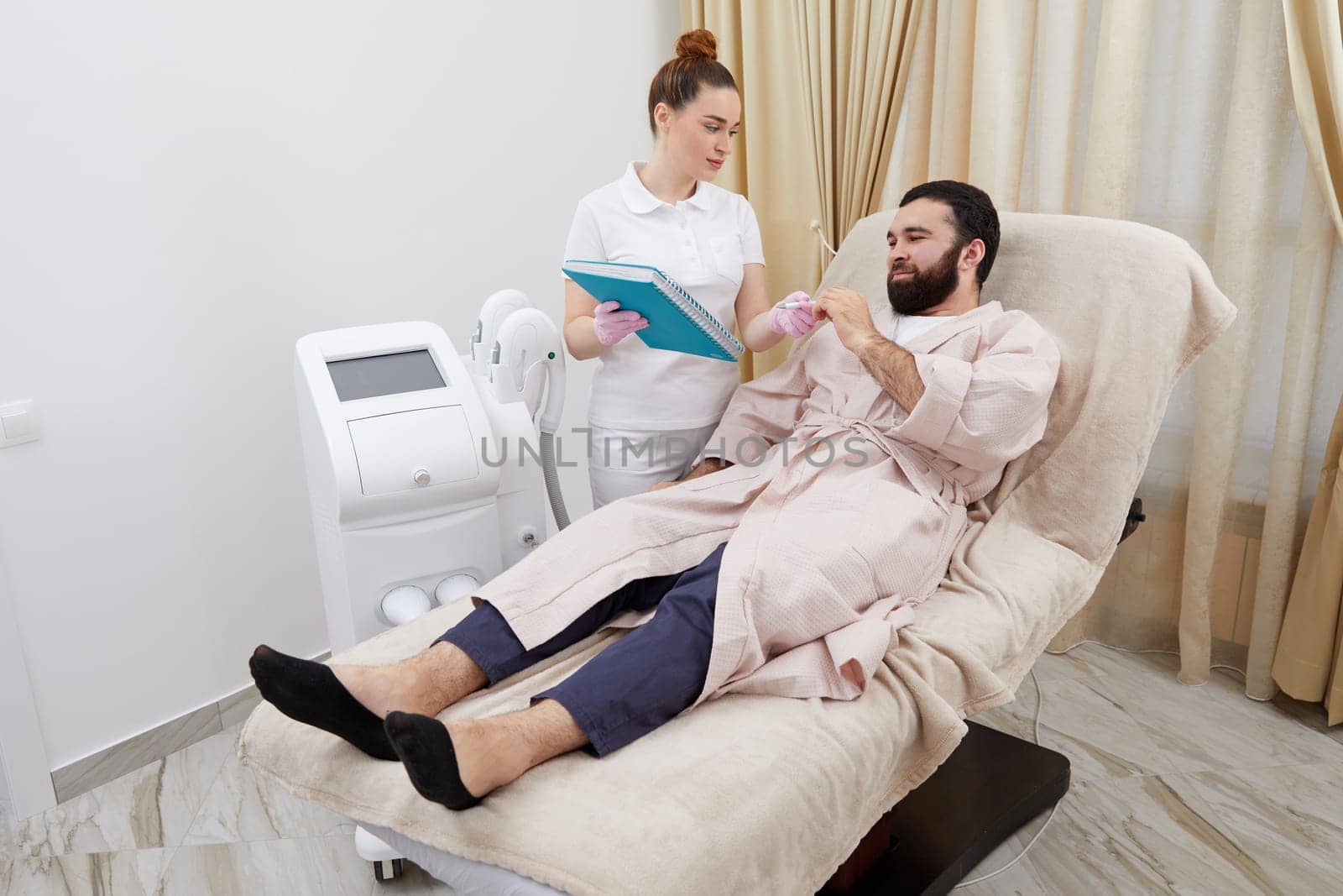 Smiling lady shows paper to man client sitting in comfortable armchair in cosmetological clinic