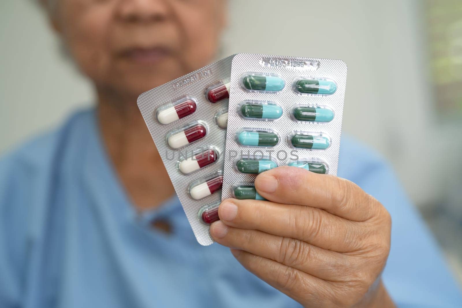 Asian senior woman patient holding antibiotics capsule pills in blister packaging for treatment infection patient in hospital, Pharmacy drugstore concept.