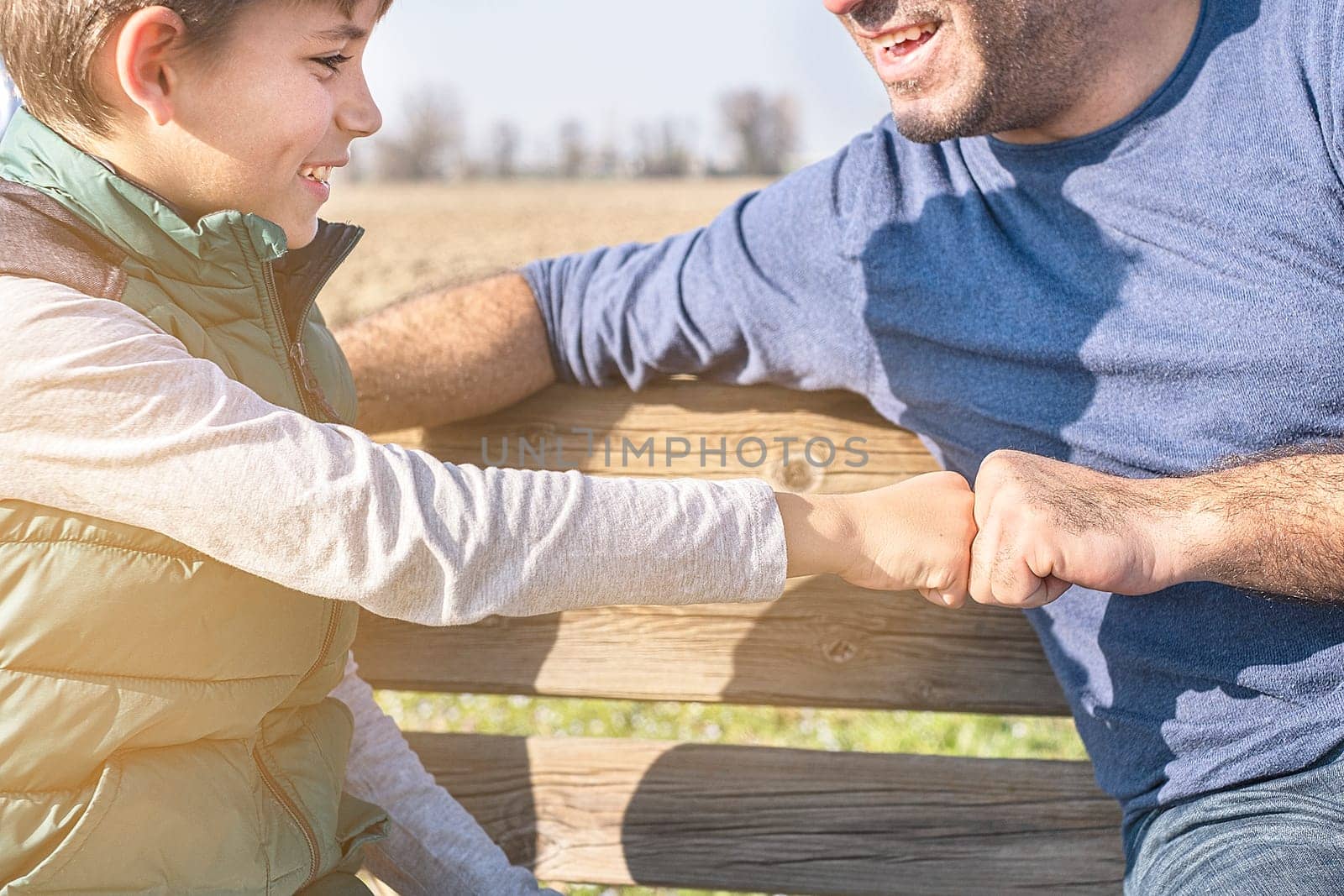 Arms of son and father fist bumping in open space.