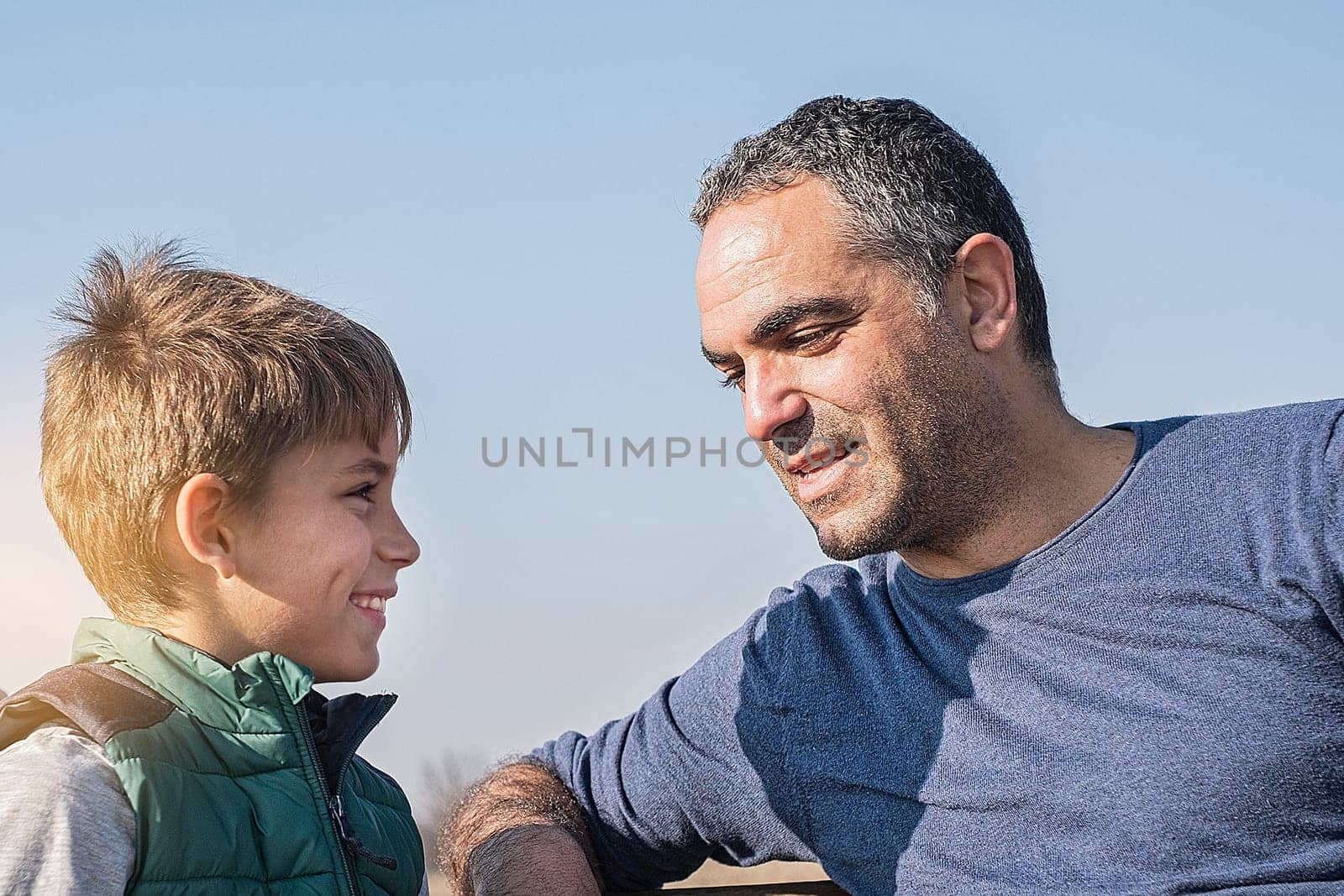 father gesturing and talking with teenager son in park on sky background