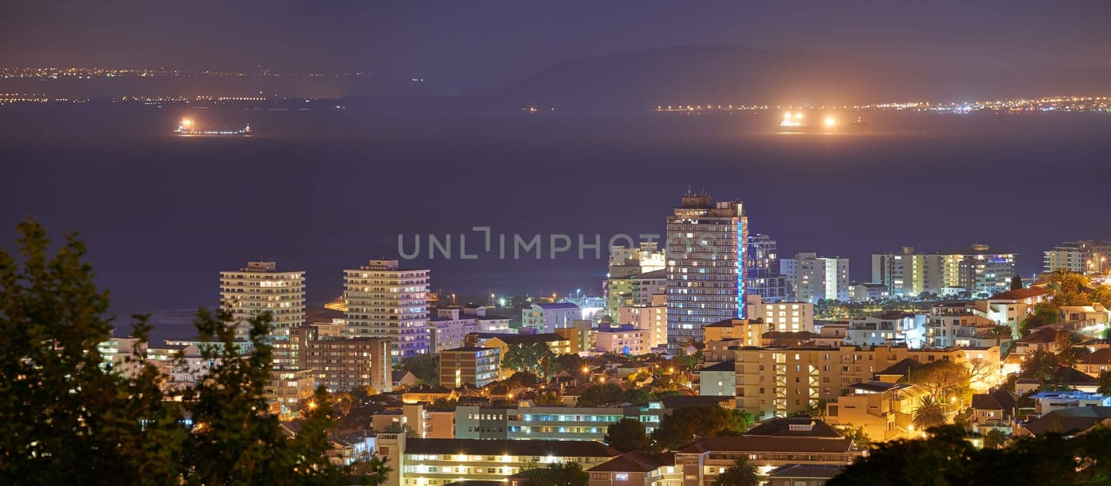 Harbour, buildings and city at night with lights, urban development and streets. Dark, travel and outdoor residential architecture of downtown with ocean or sea water in the evening with a skyline