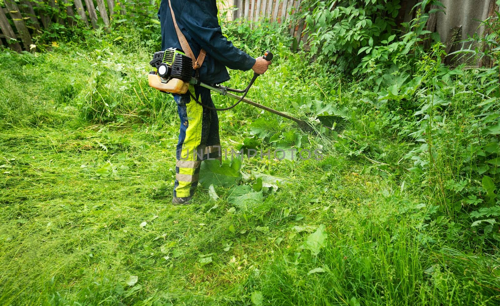 A man in a protective suit mows the grass, a mower close-up. Lawn care near the house, garden