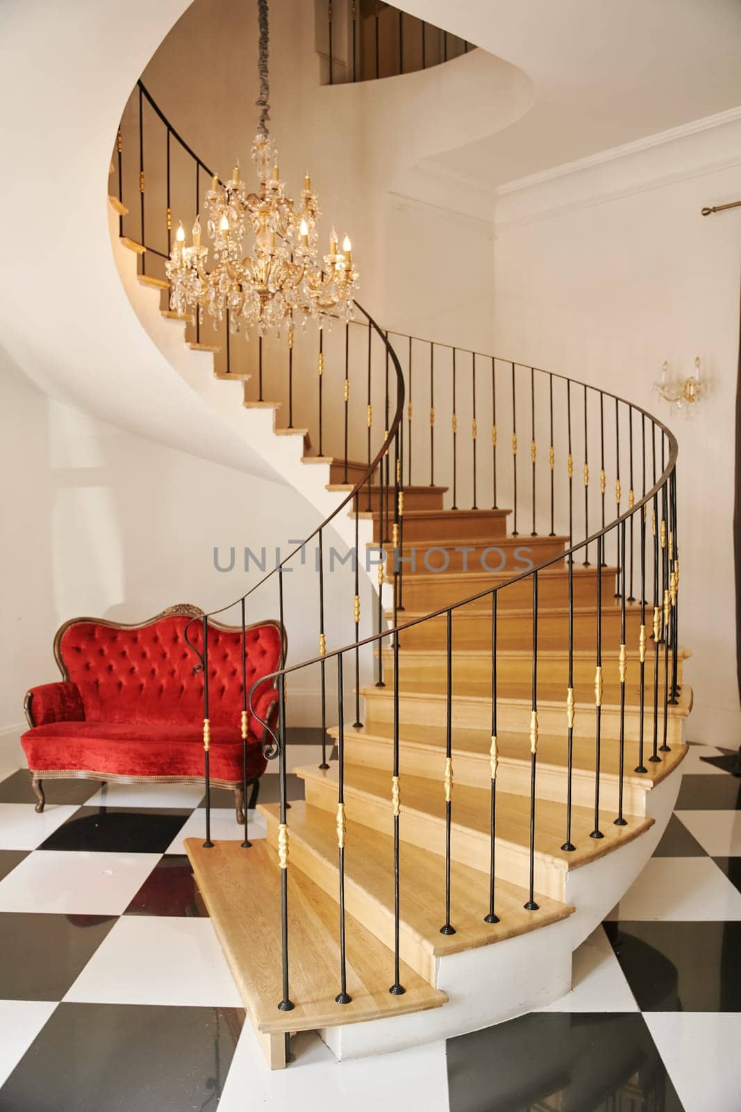 Hall with spiral staircase, glass chandelier and red sofa downstairs. High quality photo