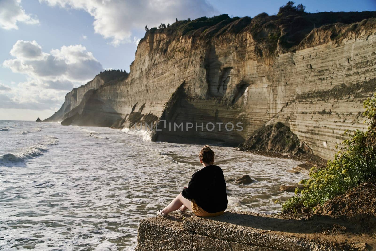 Young woman sits on a stone and admires the sea and rocks. High quality photo