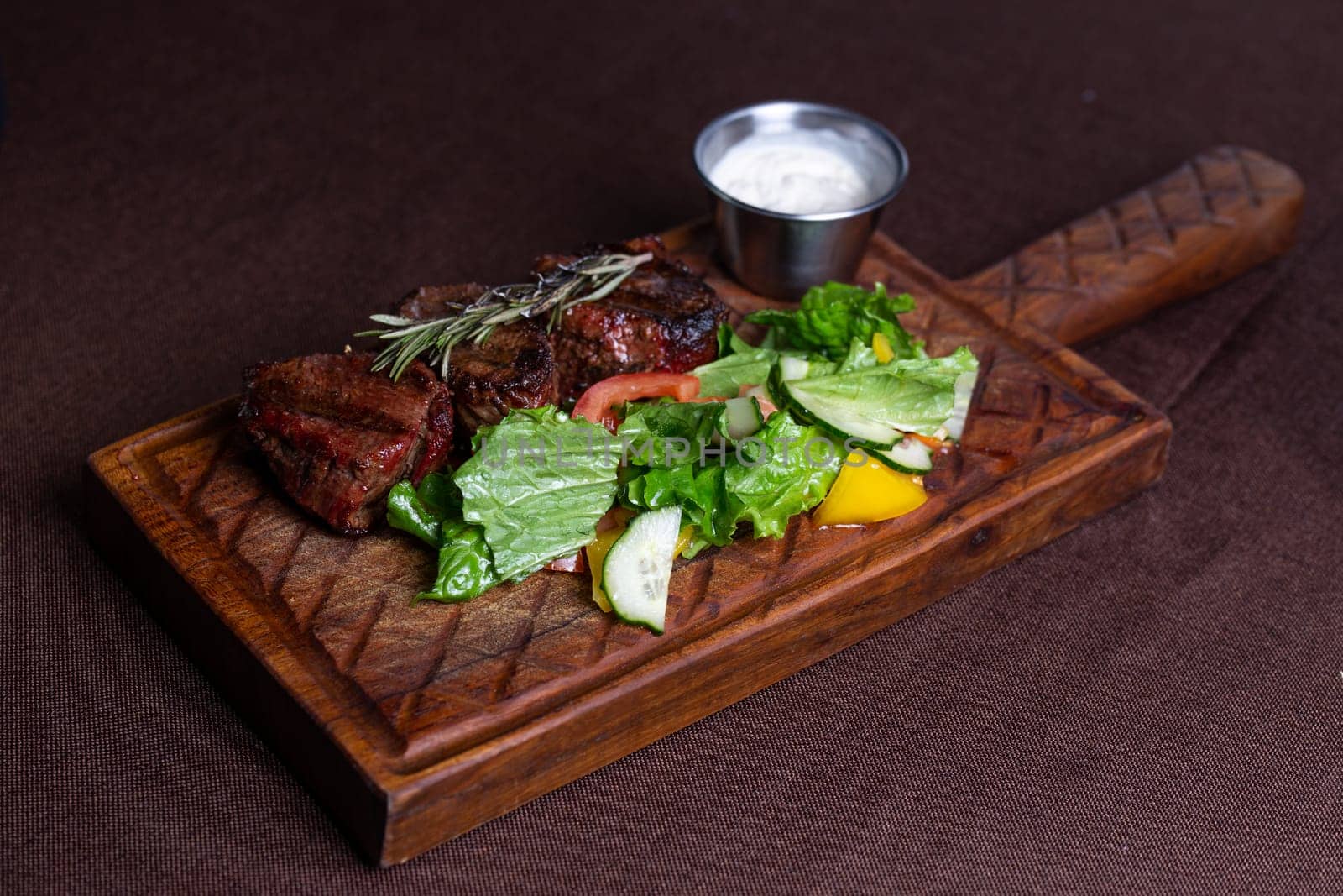 juicy beef steak with herbs and sauce on a wooden board.