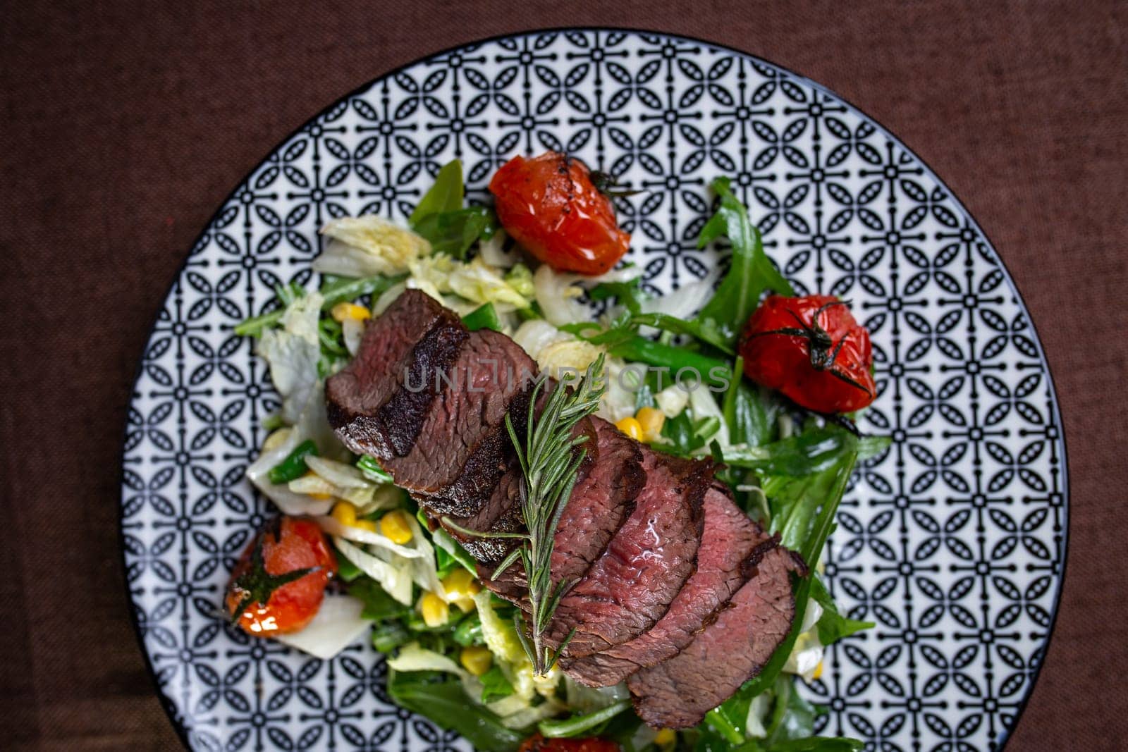 top view juicy sliced pieces of beef on a plate with herbs and tomatoes. by Pukhovskiy