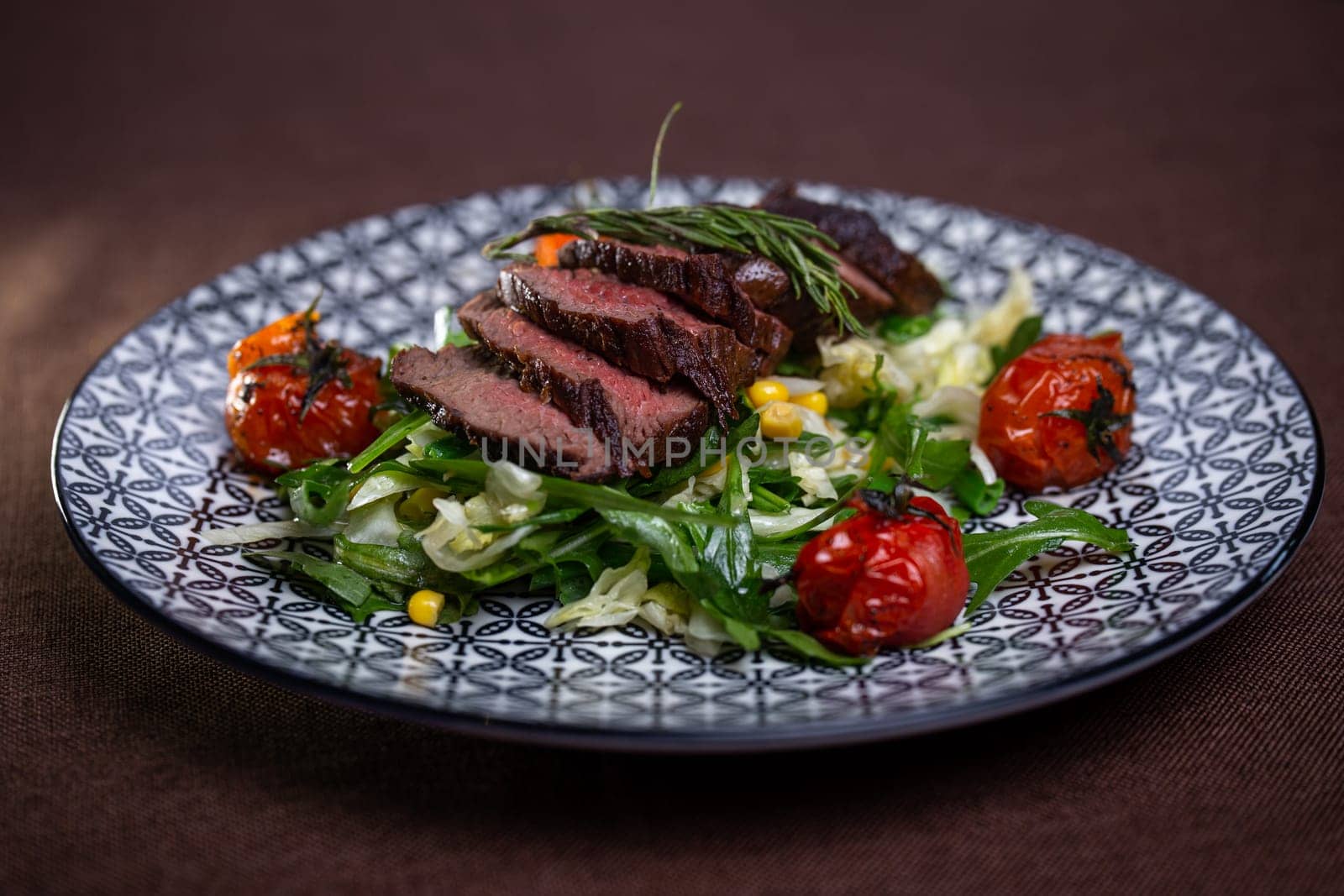 juicy cut piece of beef close-up on a plate with herbs and tomatoes.