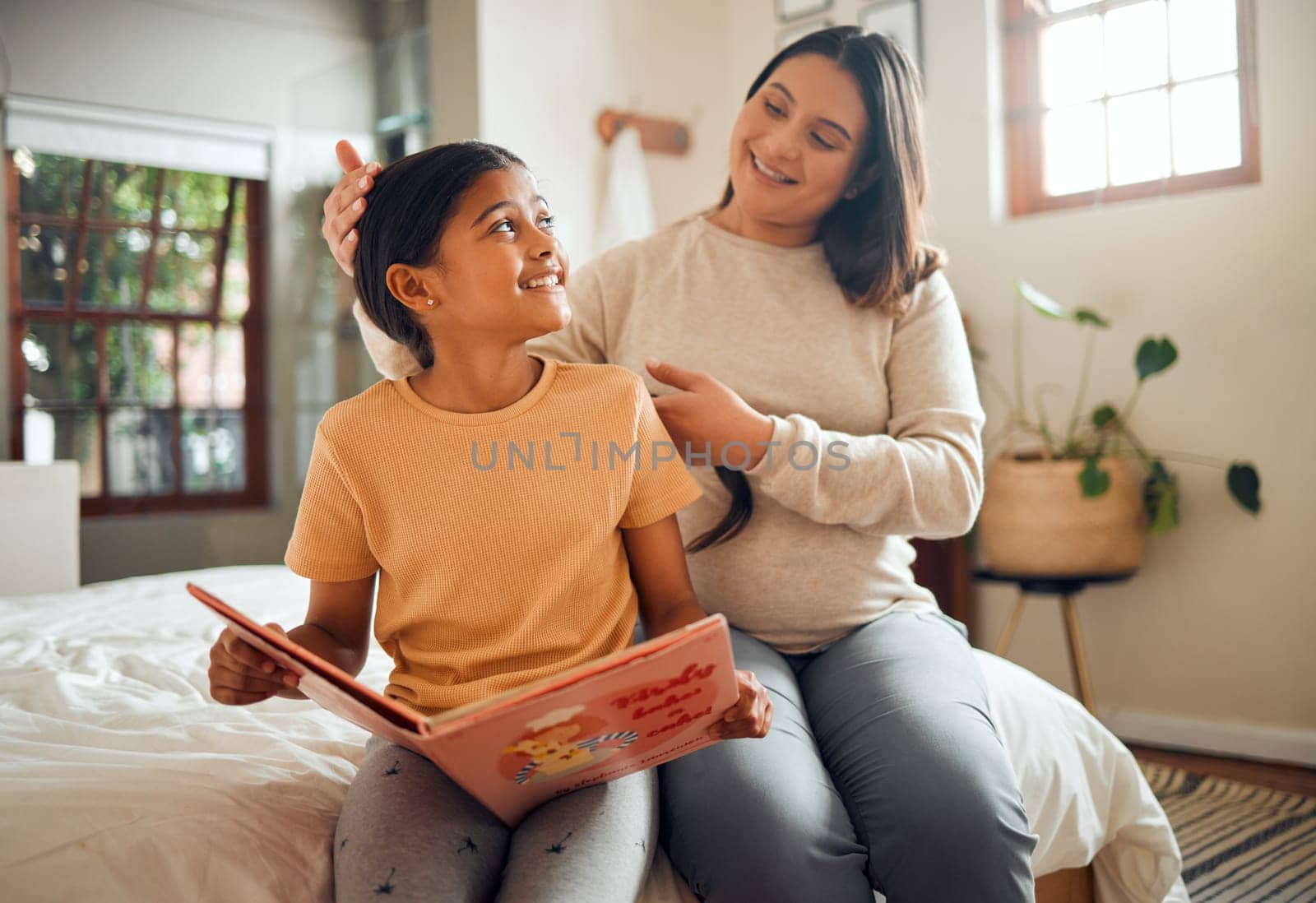 Family, book or learning and a girl reading in a bedroom with her mom playing with her hair in their home. Books, education and love with a mother and daughter bonding while sitting on a bed together.