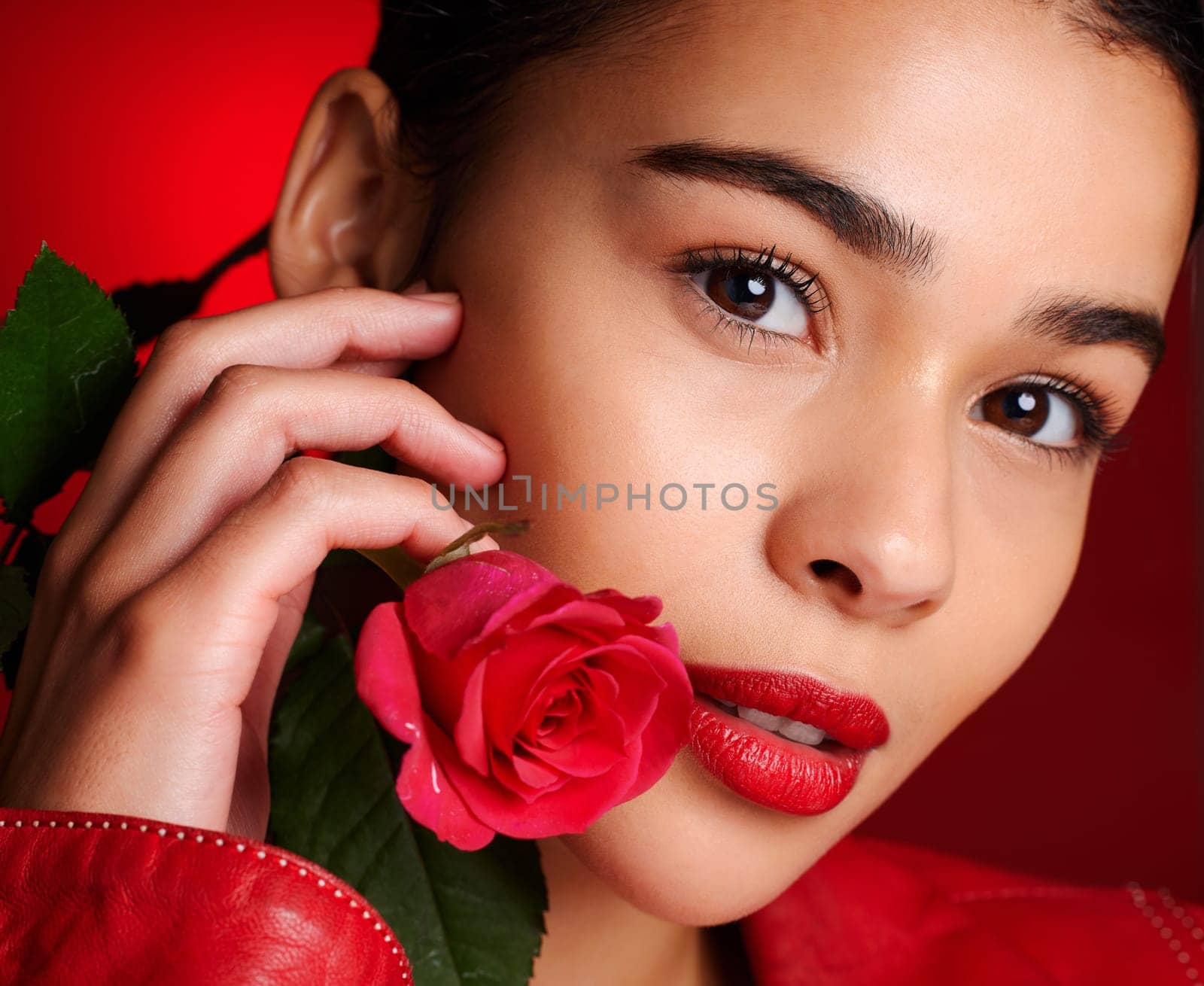 Portrait, beauty and red rose with a model woman holding a flower in studio on a wall background for valentines day. Face, romance and love with an attractive young female posing to promote dating.