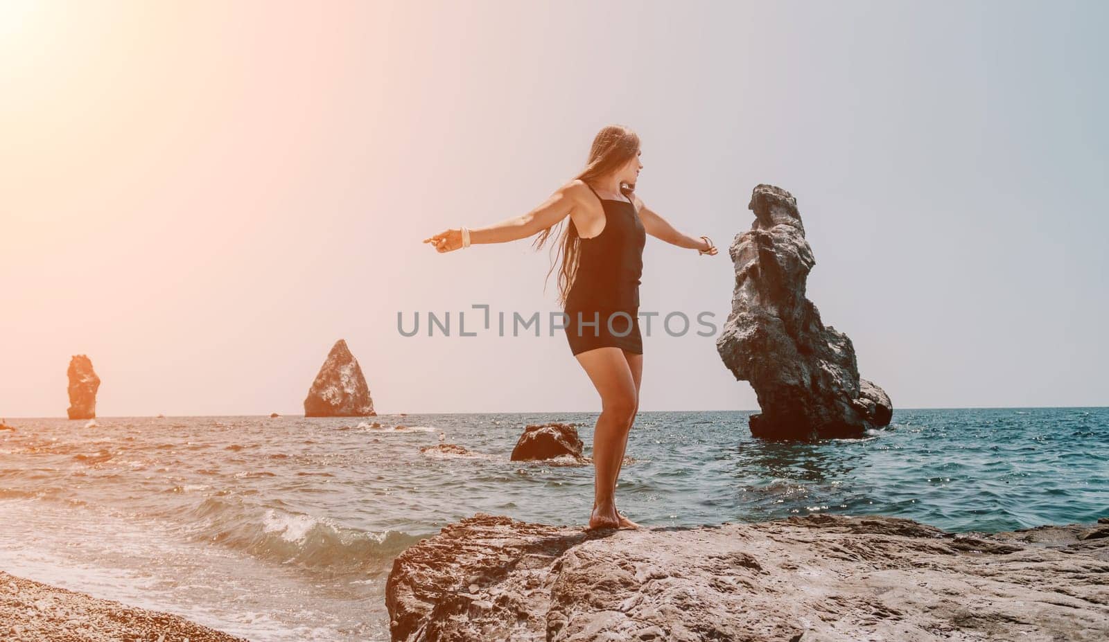 Woman travel sea. Young Happy woman in a long red dress posing on a beach near the sea on background of volcanic rocks, like in Iceland, sharing travel adventure journey