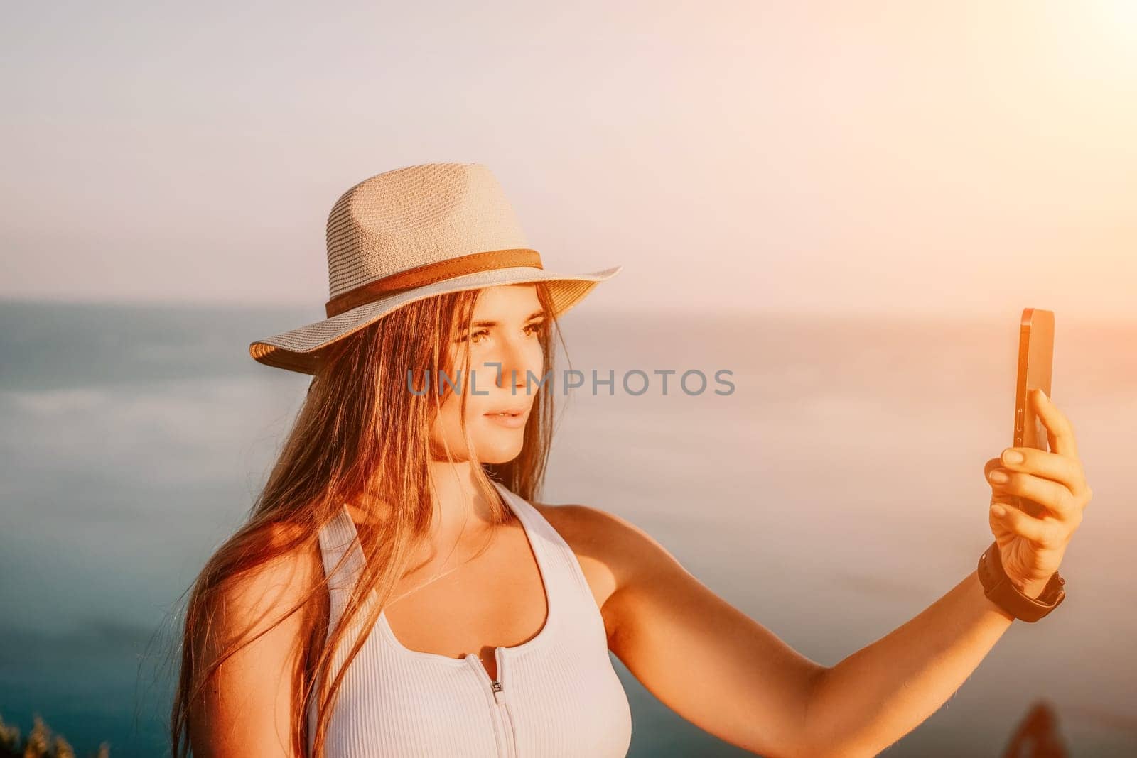 Woman travel sea. Happy tourist in hat enjoy taking picture outdoors for memories. Woman traveler posing on the beach at sea surrounded by volcanic mountains, sharing travel adventure journey