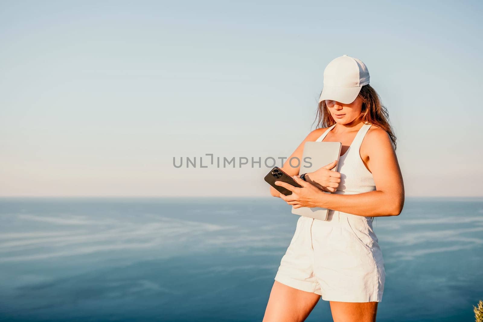 Digital nomad, Business woman working on laptop by the sea. Pretty lady typing on computer by the sea at sunset, makes a business transaction online from a distance. Freelance, remote work on vacation